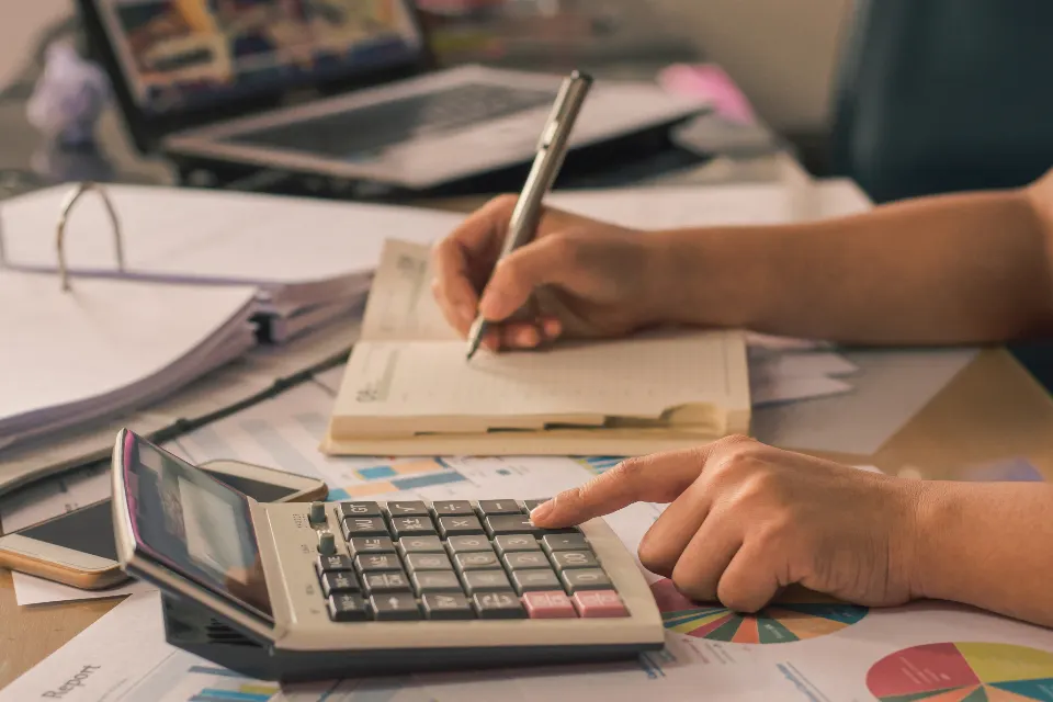 Manos anotando cifras junto a una calculadora y documentos
