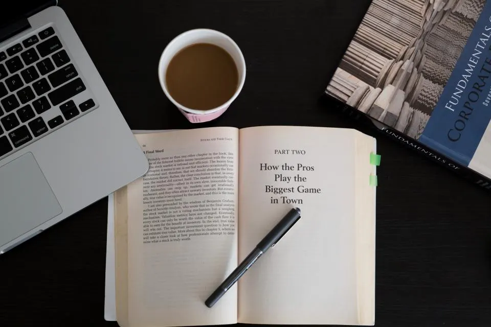 Libro abierto, bolígrafo, café y portátil sobre una mesa de estudio